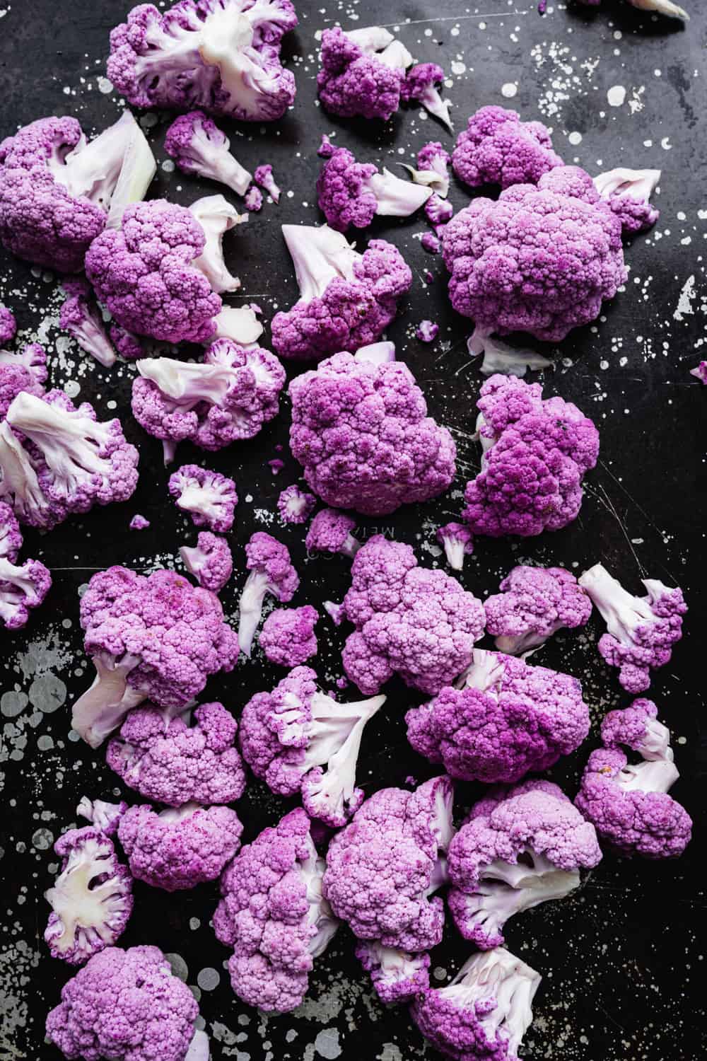 purple cauliflower florets on a black baking sheet