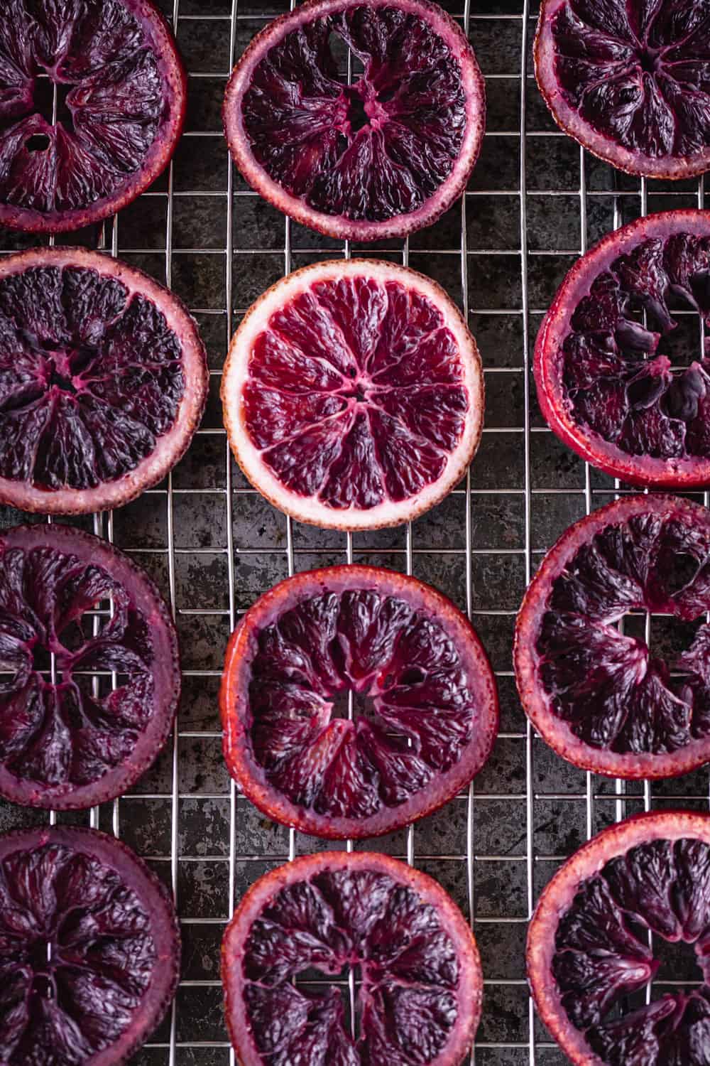 Candied blood orange slices drying on a wire rack on top of a sheet pan; overhead shot