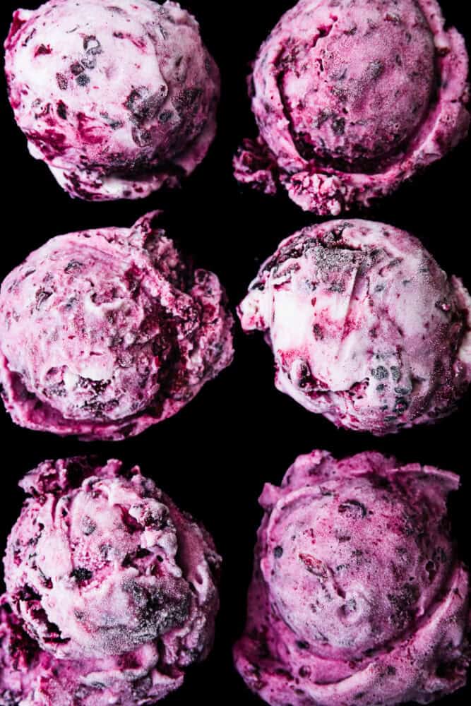 Six scoops of purple blackberry cheesecake ice cream with blackberry swirls, overhead close-up on a black background