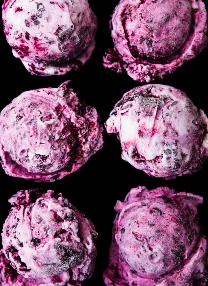 Six scoops of purple blackberry cheesecake ice cream with blackberry swirls, overhead close-up on a black background