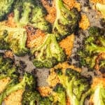 Overhead close-up of cheesy smashed broccoli roasted until slightly charred and crispy, with melted crispy cheese under it on a baking sheet.