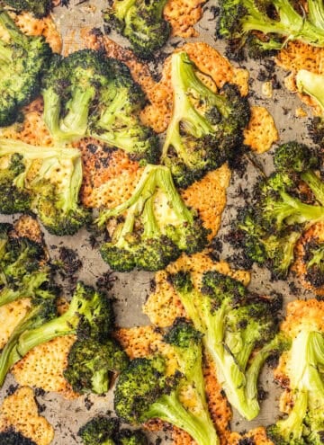 Overhead close-up of cheesy smashed broccoli roasted until slightly charred and crispy, with melted crispy cheese under it on a baking sheet.