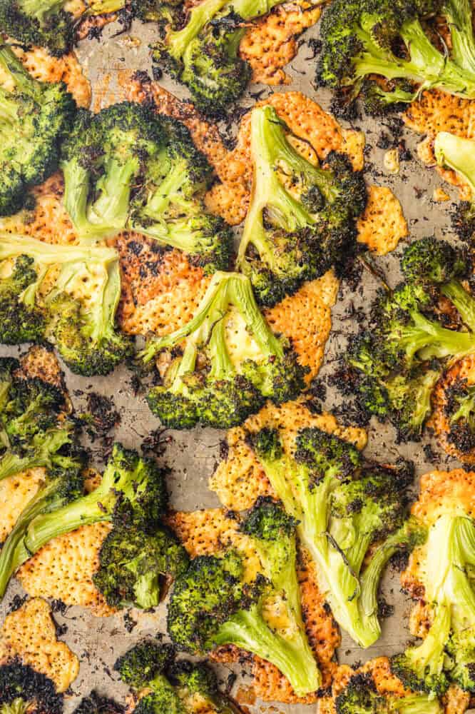 Overhead close-up of cheesy smashed broccoli roasted until slightly charred and crispy, with melted crispy cheese under it on a baking sheet.